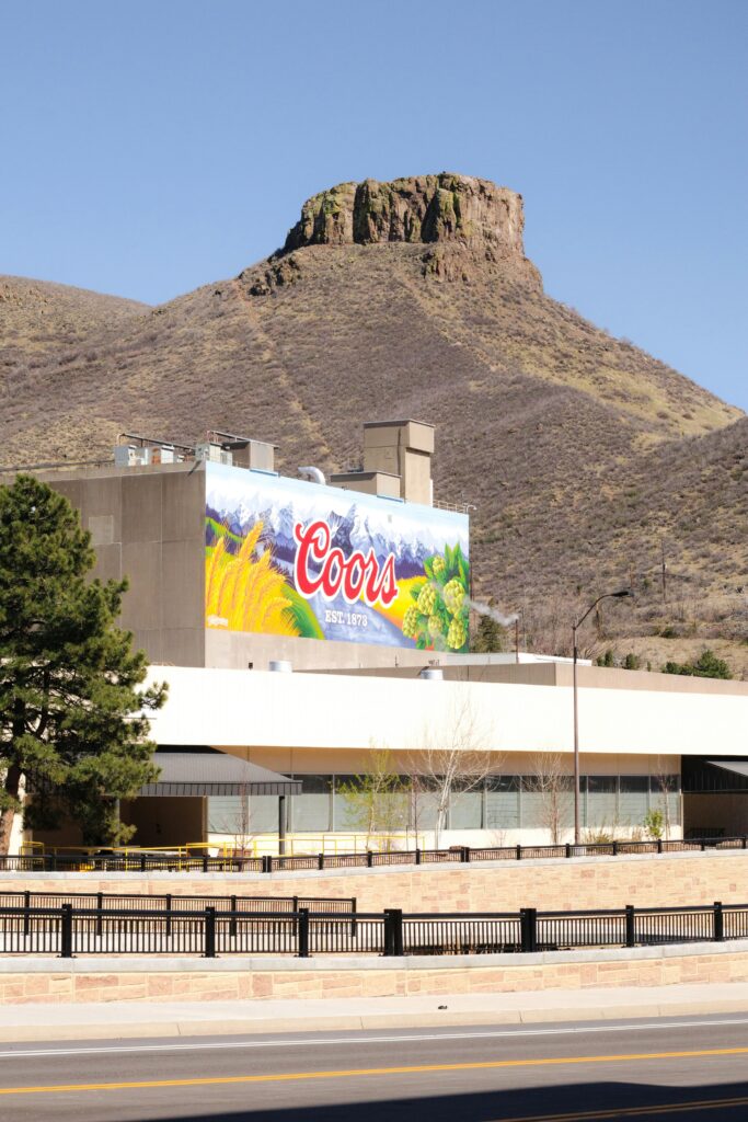 Coors brewery building with prominent mountain in the background under a clear blue sky.